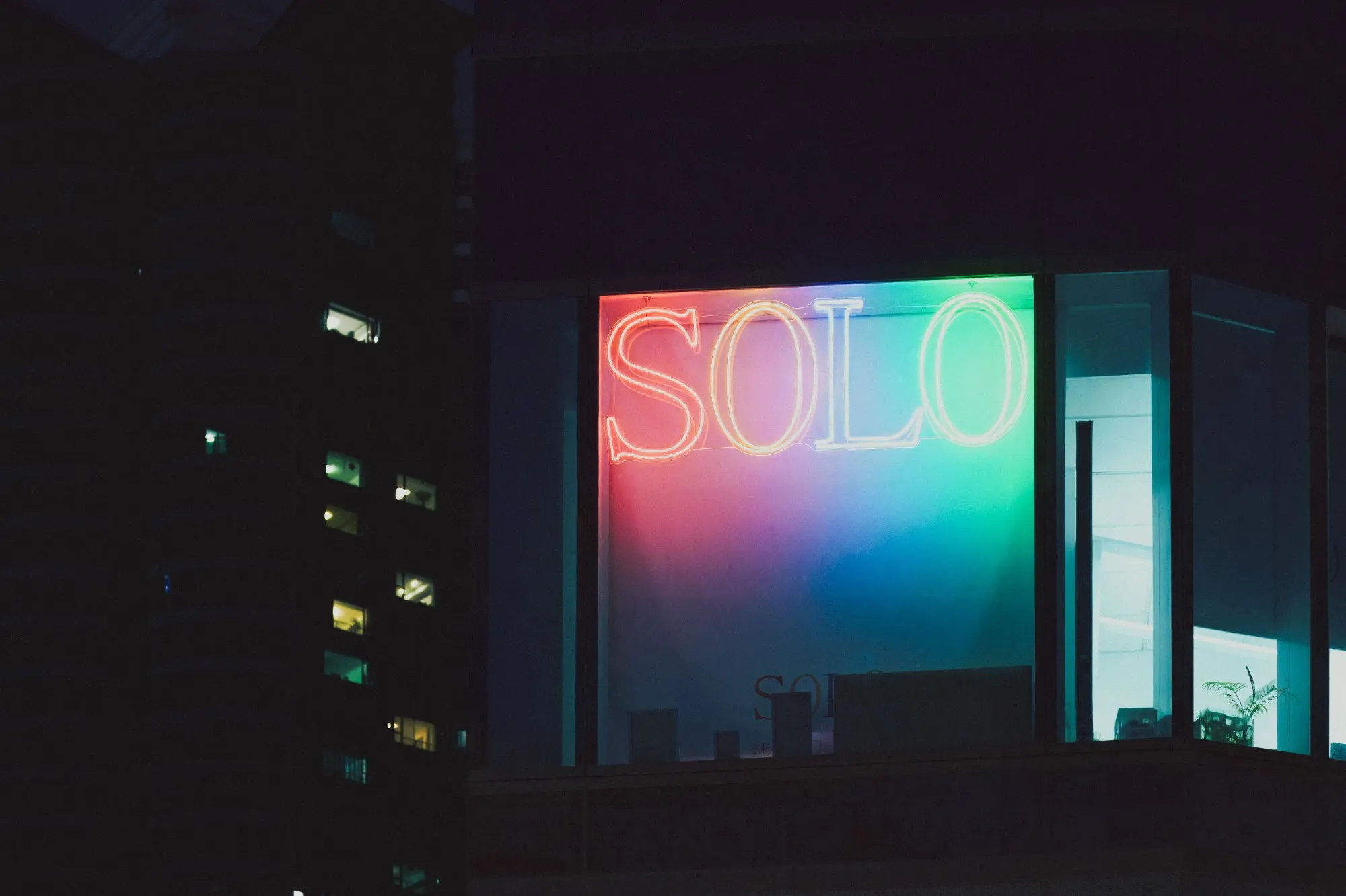 Een neonbord met het woord SOLO in een verlicht raam van een donker kantoorgebouw.