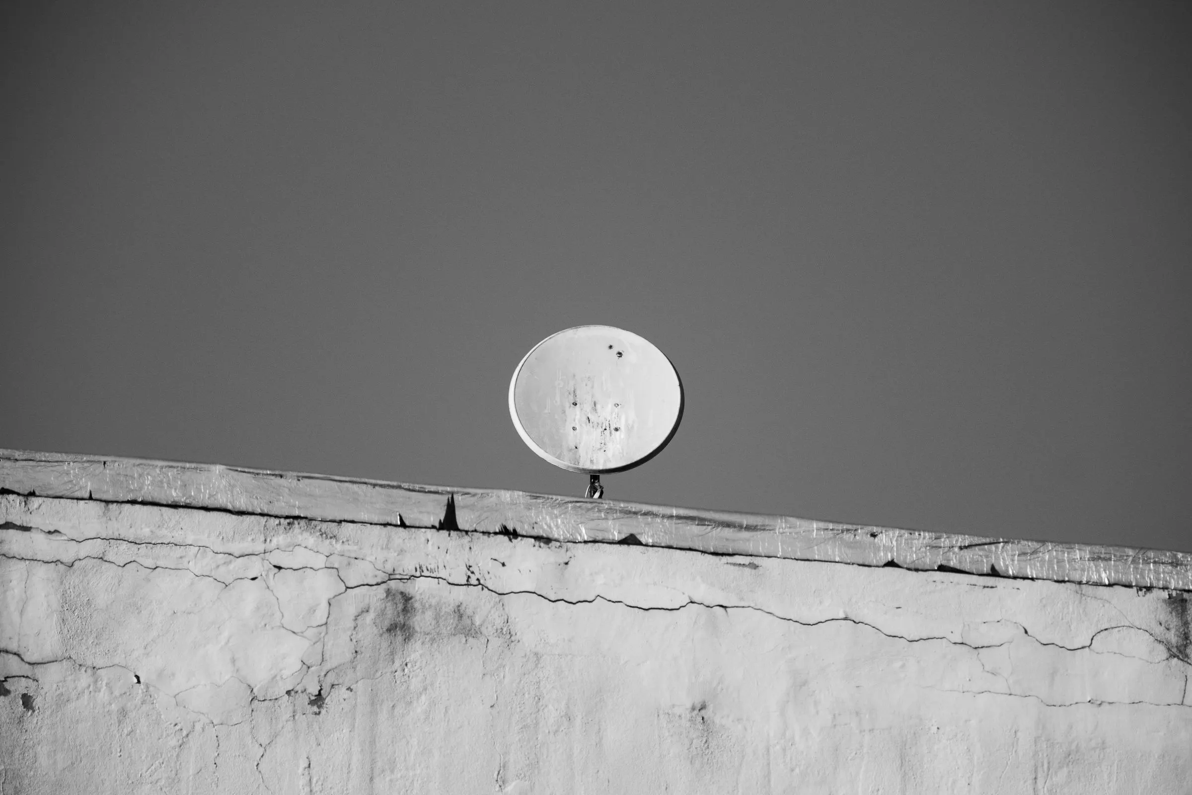 Twee schotelantennes op een dak tegen een lege lucht, in zwart-wit.